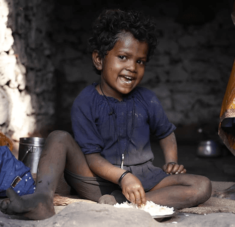 A child smiling while sharing a meal, representing the foundation’s food and care programs.
