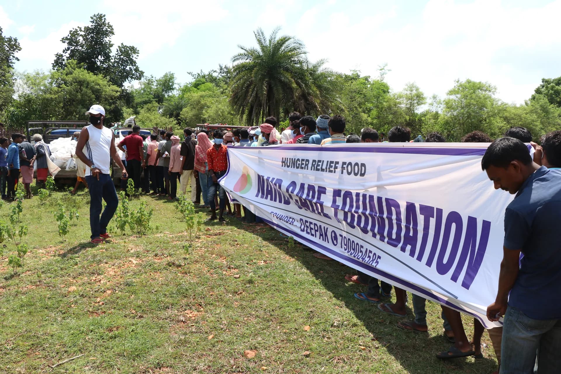 Villagers queuing beside a Nand Care Foundation hunger relief banner