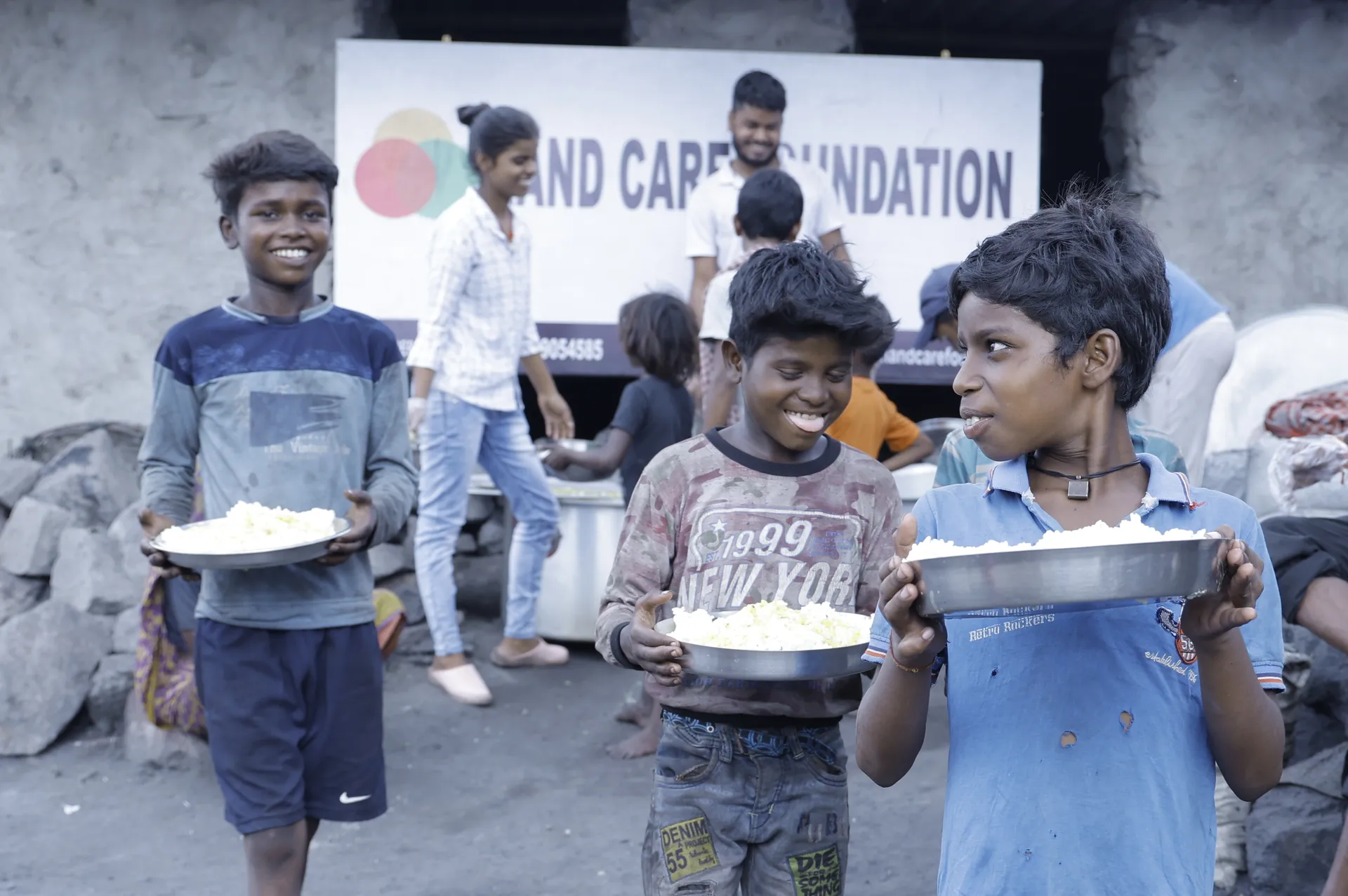 Children holding plates of food in front of a Nand Care Foundation banner