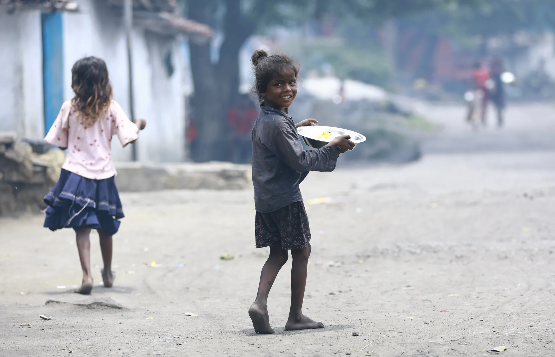 Two girls walking down a village road, one carrying a plate of food