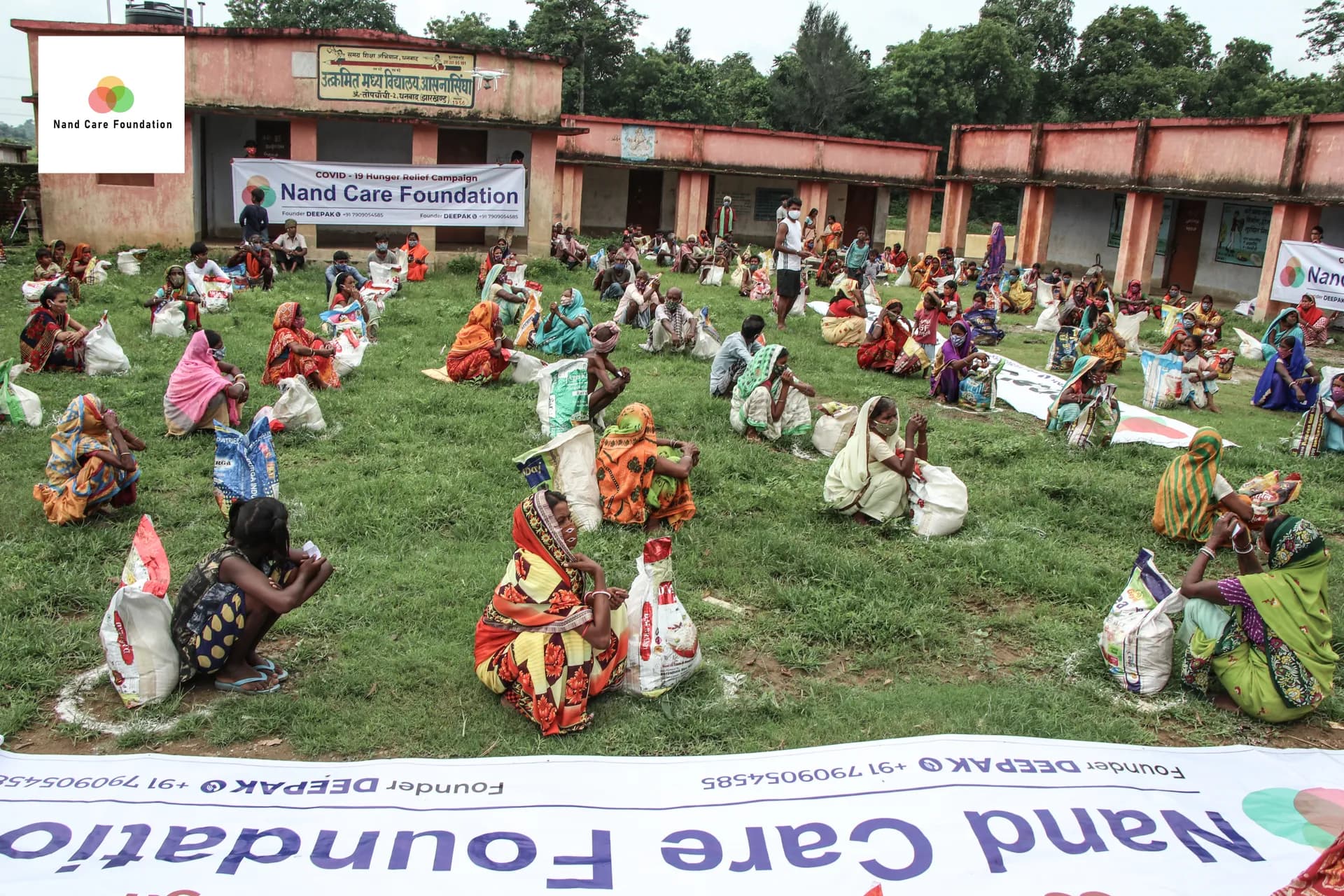 Women seated in rows on a field for a ration distribution