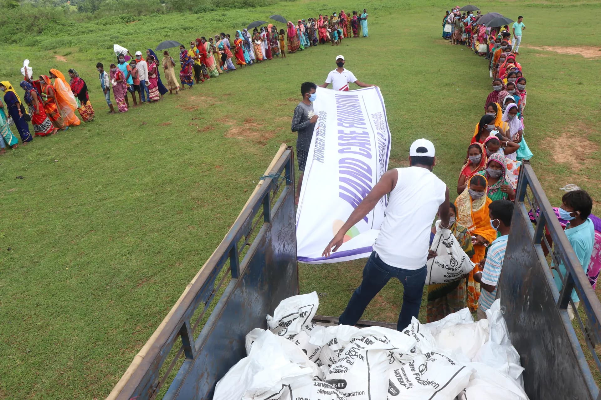 Volunteers unloading ration sacks from a truck while villagers queue
